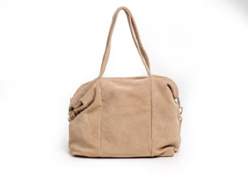 Beżowa zamszowa torebka Iris Beige z haftowanym monogramem na tle jasnej tkaniny